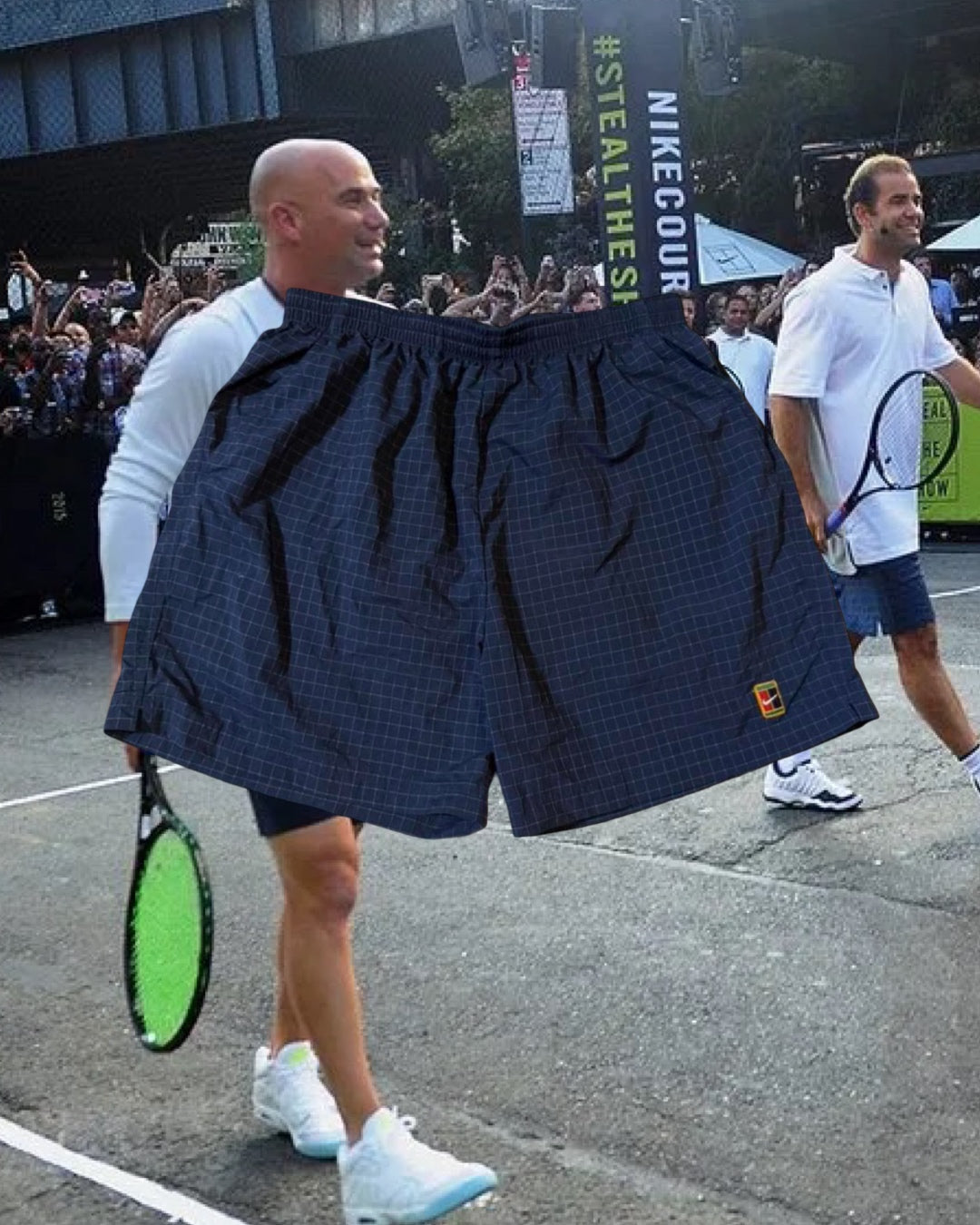 A player holds a pair of checked tennis shorts up to a packed street-court crowd