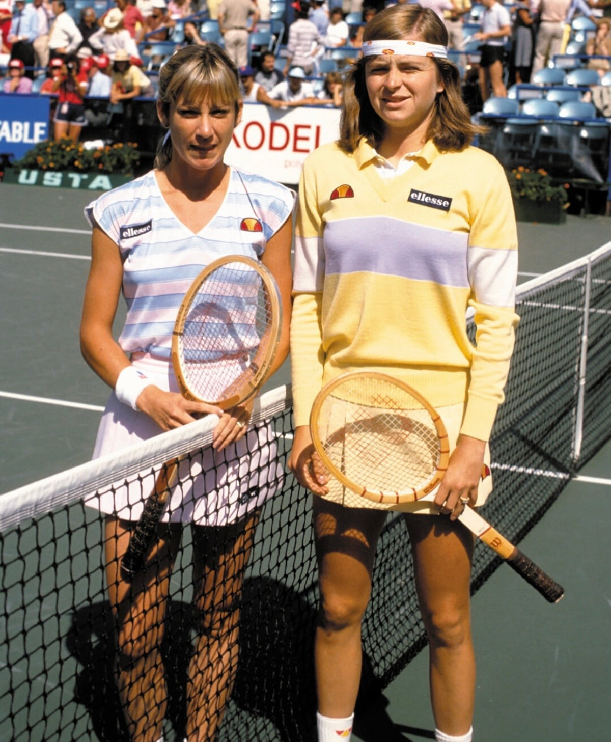 Two players meet at the net in striped and pastel knitwear, wooden rackets in hand