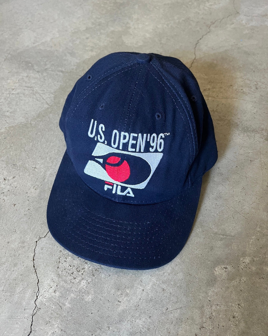 Navy US Open '96 Fila cap resting on concrete